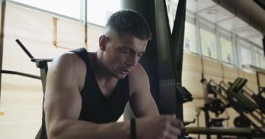 Profesyonel kaslı sporcu şortlu vücut geliştirici portresi kapalı spor salonundaki bankta oturuyor.