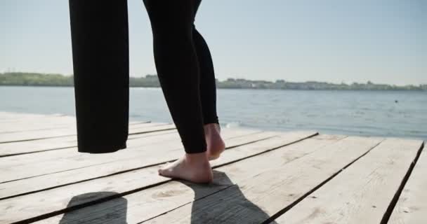 Ung blond kvinna praktiserar yoga på träkajen vid sjön. Singel sport hälsosam träning på naturen vid soligt väder — Stockvideo