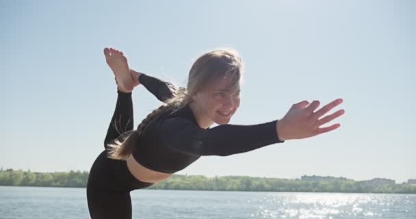 Νεαρή Ξανθιά που κάνει γιόγκα στην ξύλινη κουκέτα της λίμνης. Ενιαία άθλημα υγιή εκπαίδευση στη φύση σε ηλιόλουστο καιρό — Αρχείο Βίντεο