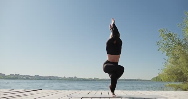 Ung blond kvinna praktiserar yoga på träkajen vid sjön. Singel sport hälsosam träning på naturen vid soligt väder — Stockvideo