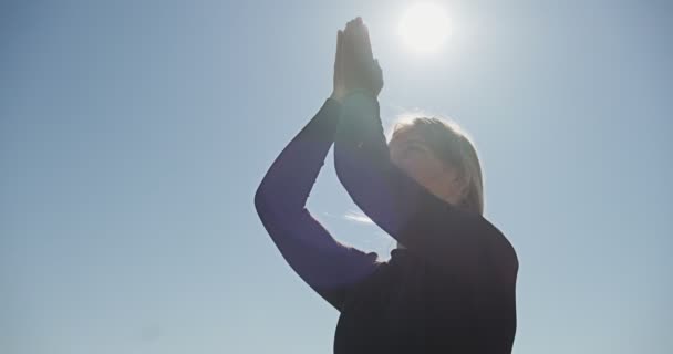 Junge blonde Frau praktiziert Yoga auf dem hölzernen Liegeplatz am See. Gesundes Einzeltraining in der Natur bei sonnigem Wetter — Stockvideo