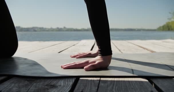 年轻的金发女人在湖边的木床上练习瑜伽。在阳光普照的天气下进行关于自然的单项运动健康训练 — 图库视频影像