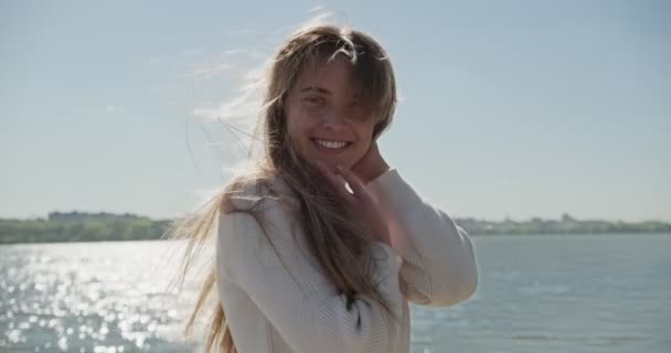 Портрет молодой привлекательной женщины, улыбающейся и смотрящей в камеру. Весело красивая женщина возле озера в солнечную погоду. Закрыть — стоковое видео