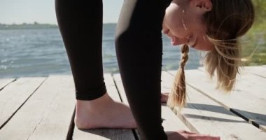 Genç sarışın kadın göldeki ahşap ranzada yoga yapıyor. Güneşli havalarda tek spor doğa üzerine sağlıklı eğitim