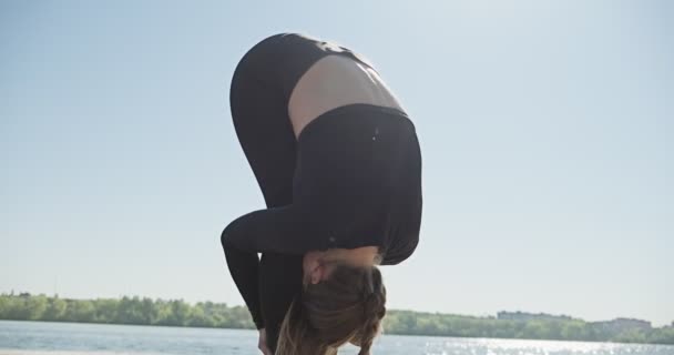 Jonge blonde vrouw die yoga beoefent op de houten ligplaats aan het meer. Single sport gezonde training op de natuur bij zonnig weer — Stockvideo