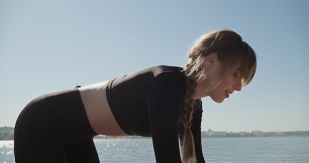 Jovem loira praticando ioga no cais de madeira no lago. Único esporte treinamento saudável sobre a natureza em tempo ensolarado — Vídeo de Stock