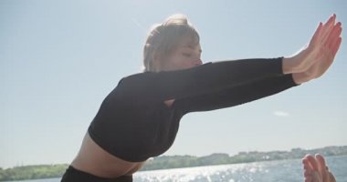 Genç sarışın kadın göldeki ahşap ranzada yoga yapıyor. Güneşli havalarda tek spor doğa üzerine sağlıklı eğitim