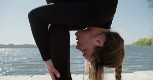 Giovane donna bionda che pratica yoga sul letto di legno al lago. Singolo sport sano allenamento sulla natura al tempo soleggiato — Video Stock