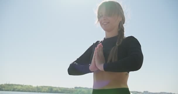 Jeune femme blonde pratiquant le yoga sur la couchette en bois au lac. Entraînement sportif unique sain sur la nature par beau temps — Video