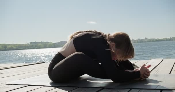 Jovem loira praticando ioga no cais de madeira no lago. Único esporte treinamento saudável sobre a natureza em tempo ensolarado — Vídeo de Stock