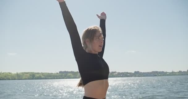 Ung blond kvinna praktiserar yoga på träkajen vid sjön. Singel sport hälsosam träning på naturen vid soligt väder — Stockvideo