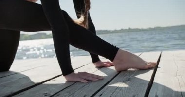 Genç sarışın kadın göldeki ahşap ranzada yoga yapıyor. Güneşli havalarda tek spor doğa üzerine sağlıklı eğitim