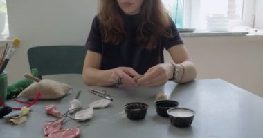 Kadın oyuncak bebek seramik parçası yapıyor. Kadın evde oturuyor ve masada bebek için kulak yapıyor. Çömlek bebekleri parçaları, el yapımı ve yaratıcı yetenekler