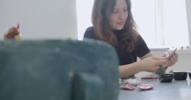Kadın oyuncak bebek seramik parçası yapıyor. Kadın evde oturuyor ve masada bebek için kulak yapıyor. Çömlek bebekleri parçaları, el yapımı ve yaratıcı yetenekler