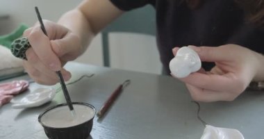 Kadın oyuncak bebek seramiği yapıyor. Kadın evde oturuyor ve masada bebek için kulak yapıyor. Çömlek bebekleri parçaları, el yapımı ve yaratıcı yetenekler