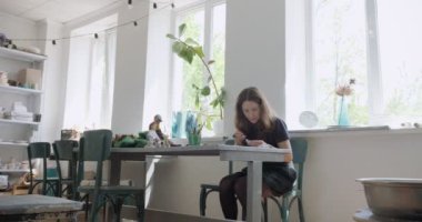 Kadın oyuncak bebek seramik parçası yapıyor. Kadın evde oturuyor ve masada bebek için kulak yapıyor. Çömlek bebekleri parçaları, el yapımı ve yaratıcı yetenekler