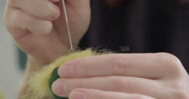Masada yün oyuncak bebek yapan bir kadın var. Kadın evde oturup meşe bebek yapıyor. İğne Keçeli El yapımı ve yaratıcı yetenekler