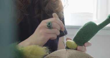 Masada yün oyuncak bebek yapan bir kadın var. Kadın evde oturup meşe bebek yapıyor. İğne Keçeli El yapımı ve yaratıcı yetenekler
