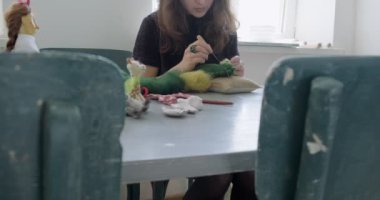 Masada yün oyuncak bebek yapan bir kadın. Kadın evde oturup meşe bebek yapıyor. İğne Keçeli El yapımı ve yaratıcı yetenekler