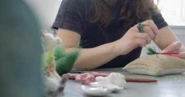 Masada yün oyuncak bebek yapan bir kadın var. Kadın evde oturup meşe bebek yapıyor. İğne Keçeli El yapımı ve yaratıcı yetenekler