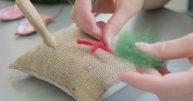 Masada yün oyuncak bebek yapan bir kadın var. Kadın evde oturup meşe bebek yapıyor. İğne Keçeli El yapımı ve yaratıcı yetenekler