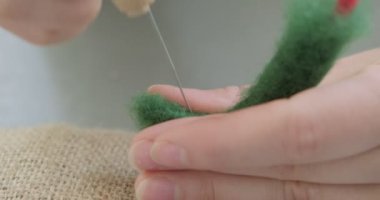 Masada yün oyuncak bebek yapan bir kadın var. Kadın evde oturup meşe bebek yapıyor. İğne Keçeli El yapımı ve yaratıcı yetenekler