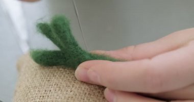 Masada yün oyuncak bebek yapan bir kadın var. Kadın evde oturup meşe bebek yapıyor. İğne Keçeli El yapımı ve yaratıcı yetenekler