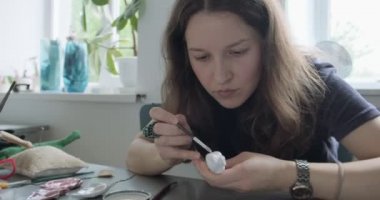 Kadın oyuncak bebek seramik parçası yapıyor. Kadın evde oturuyor ve masada bebek için kulak yapıyor. Çömlek bebekleri parçaları, el yapımı ve yaratıcı yetenekler