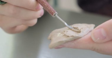 Kadın oyuncak bebek seramiği yapıyor. Kadın evde oturuyor ve masada bebek için kulak yapıyor. Çömlek bebekleri parçaları, el yapımı ve yaratıcı yetenekler.