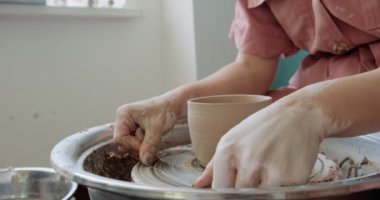 Kadın çömlekçi oturuyor ve çömlek çarkında bir fincan yapıyor. Kadın seramik bir şey yapıyor. Çömlekçilik, el yapımı ve yaratıcı beceriler