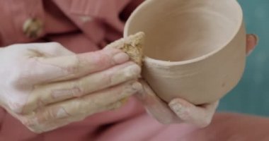 Dişi çömlekçi oturuyor ve bir fincan yapıyor. Kadın seramik bir şey yapıyor. Çömlekçilik, el yapımı ve yaratıcı beceriler