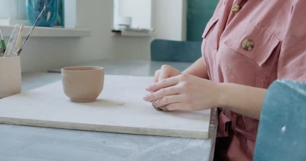 Ceramista donna seduta e fa una tazza a tavola. Donna che fa oggetti in ceramica. Lavorazione della ceramica, abilità artigianali e creative — Video Stock