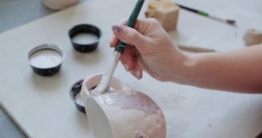 Dişi çömlekçi masada bir fırçayla boya karıştırıyor. Kadın seramik bir şey yapıyor. Çömlekçilik, el yapımı ve yaratıcı beceriler