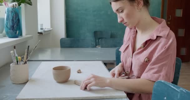 Ceramista donna seduta e fa una tazza a tavola. Donna che fa oggetti in ceramica. Lavorazione della ceramica, abilità artigianali e creative — Video Stock
