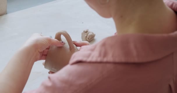 Ceramista donna seduta e fa una tazza a tavola. Donna che fa oggetti in ceramica. Lavorazione della ceramica, abilità artigianali e creative — Video Stock