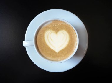 Siyah arka planda kalp sembolü olan bir fincan kahve.