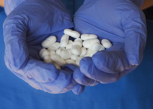 Hemşire elinde koruyucu eldivenlerle beyaz haplar tutuyor.