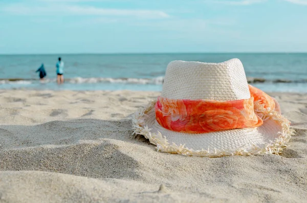 Солом'яний капелюх на пляжі з розмитими людьми і морським фоном . — стокове фото