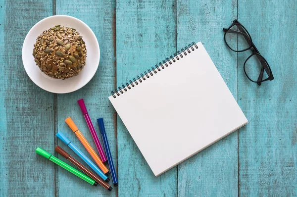 Blue wooden desk table with notebook, color pen, bread and cup o — Stock Photo, Image