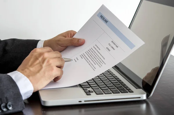 job seeker review his resume on his desk with pen and computer l