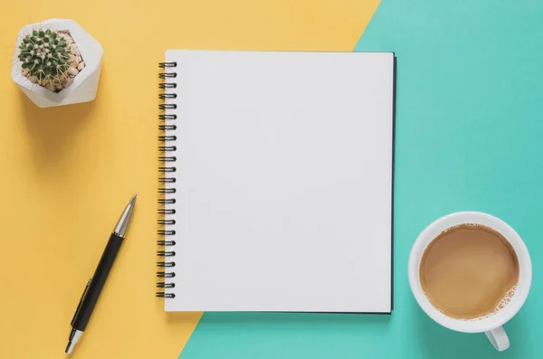 Office workplace minimal concept. Blank notebook with cup of coffee, cactus, pencil on yellow and blue background. — Stock Photo, Image