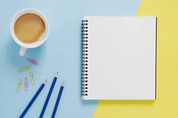 办公室工作场所最小概念。空白的笔记本，杯咖啡，铅笔，纸夹在黄色和蓝色的背景上. — 图库照片
