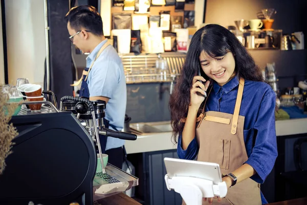 Asian barista talking order by phone in her shop. Cafe restauran