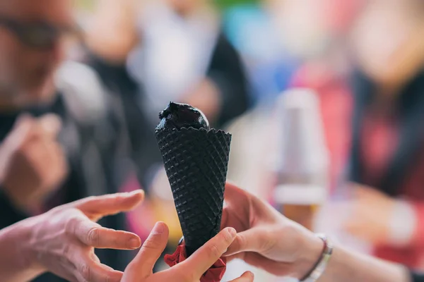 Black ice cream is the new treat of summer. Cone with black ice cream, hit a new taste, several hands are drawn to trend. Background with colorful bokeh. Copy space — Stock Photo, Image