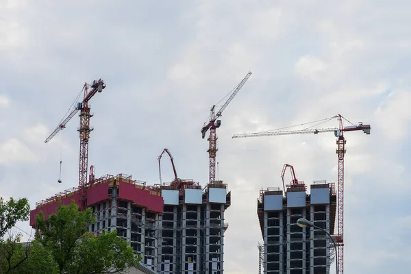 Lift torenkranen op bouwplaats tegen de achtergrond van de blauwe hemel, de nieuwe gebouwen van de huizen in de buurt van een woonwijk met bomen — Stockfoto