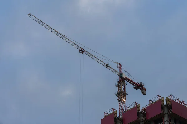 Grue à tour de construction à côté d'un bâtiment en construction sur le fond du ciel bleu avec des nuages. Avec place pour votre texte, pour une utilisation de fond — Photo