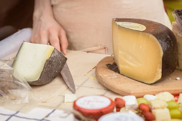 Cabeças de queijo cortadas no balcão do mercado, mãos de mulher do vendedor com faca — Fotografia de Stock