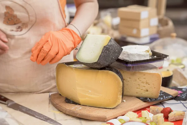 A vendedora vende queijo. Mãos femininas. Corte cabeças de queijo na placa de madeira do mercado. Foco seletivo . — Fotografia de Stock