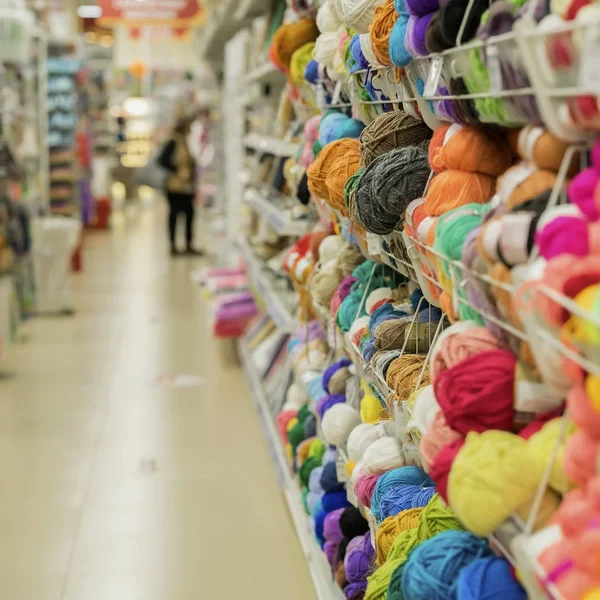 Mujer hace la elección de hilo para tejer en la tienda de bienes para la creatividad y la costura. Estantes en la tienda de costuras. Hobby, costura. Movimiento desenfocado borroso — Foto de Stock
