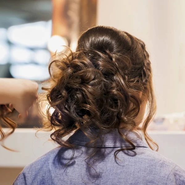 Onherkenbaar meisje terug naar ons, jonge vrouw in de spiegel bij kapper maken van kapsel, styling van lange haren in de kapsalon. Handen van meester zijn gedeeltelijk zichtbaar — Stockfoto
